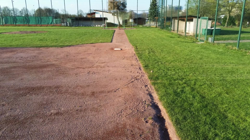 Drone flying from third base to home plate over green baseball field.