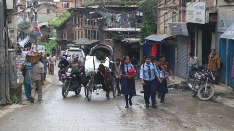 Kathmandu, Nepal - 04 11 2019: Man pulling heaving Rickshaw up road with school children and people walking in busy street in Kathmandu, Nepal