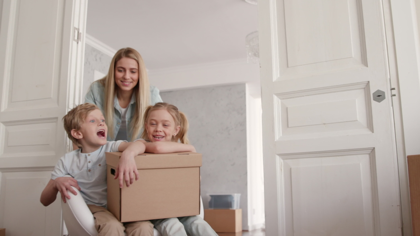 Family Group Move in Beautiful Flat in Modern Building. Two Babies Ride a Chair Inside Big Real Estate. Carton Packaging of Caucasian Small Child. Funny Adult Mom on Relocating Day or Active Unpacking Royalty-Free Stock Footage #1034046695