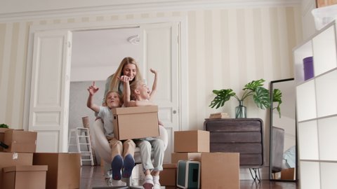 Family Group Move in Beautiful Flat in Modern Building. Two Babies Ride a Chair Inside Big Real Estate. Carton Packaging of Caucasian Small Child. Funny Adult Mom on Relocating Day or Active Unpacking