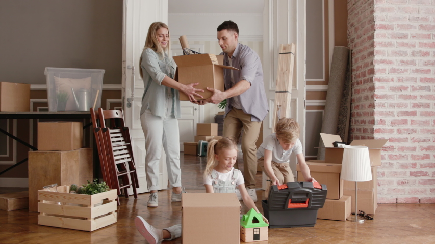 Family Moves in Modern Real Estate or Cozy Large Rent after Sale. Unpacking by Adult Dad with Furniture or Packing. Beautiful Laughing Mom at Casual Relocating. Child Emotion of Small Son and Daughter | Shutterstock HD Video #1034046710