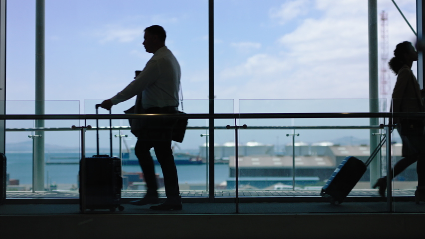 business people at busy airport pulling trolley bags arriving and departing terminal tourists travelling international walking in lobby with view of harbor port 4k footage Royalty-Free Stock Footage #1034047298