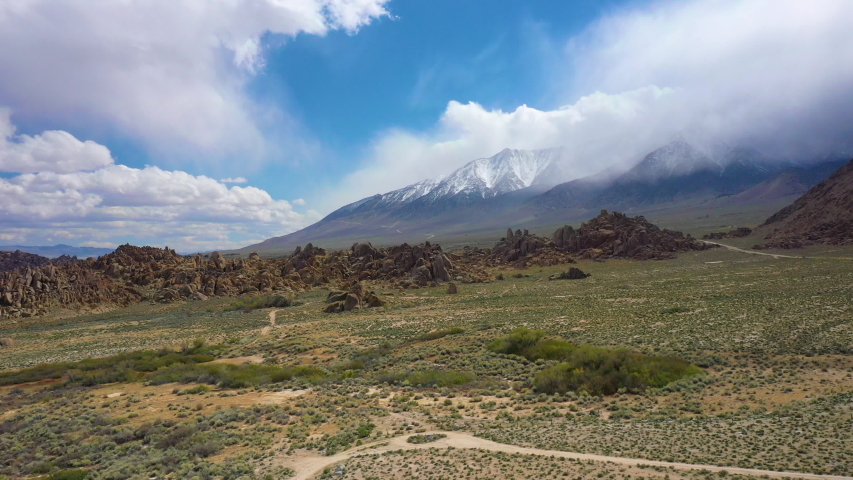 Aerial of car driving on road in Alabama Hills, California, USA. Snow-capped mountains of Eastern Sierra Nevada in the background.