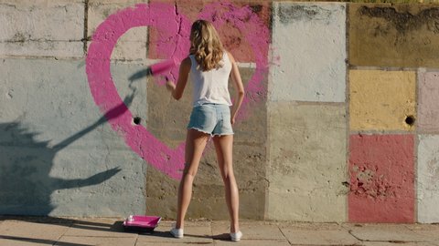 graffiti artist woman painting heart shape on wall with pink paint rebellious young girl enjoying artistic expression with peace and love concept urban street art 4k
