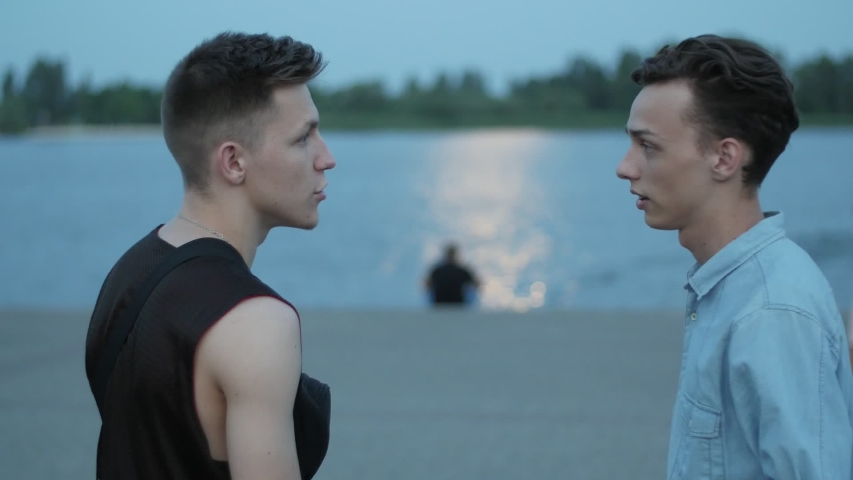 Two young friends walking to the water on the embankment at dusk, Slow motion