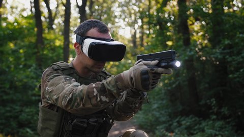 Soldier aiming with gun wearing virtual reality glasses outdoors
