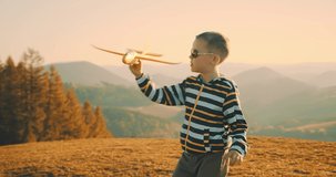 Children playing outside. Happy traveler boy playing with airplane toy on sunny day in park. 4K slow motion video. Child runs on top of mountain at sunset. Journey to the Edge of the Universe