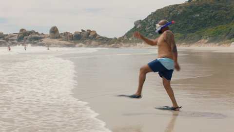 funny african american man walking on beach in sea water wearing flippers getting ready to swim enjoying summer by ocean 4k