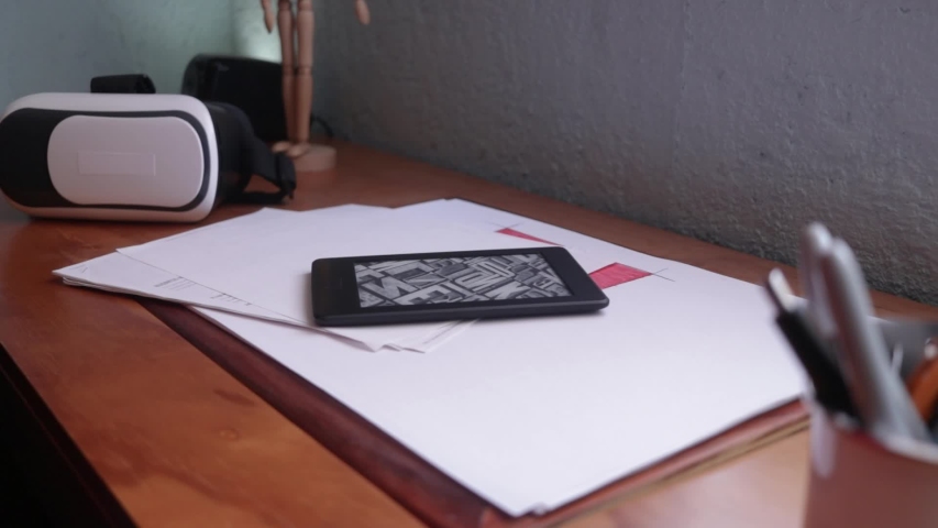 Side view. Male hand taking an ebook reader from the desk. Ebook reader on a wooden desk. Man switch off an ebook reader. Vr headset on background. 3d experience with a vr headset