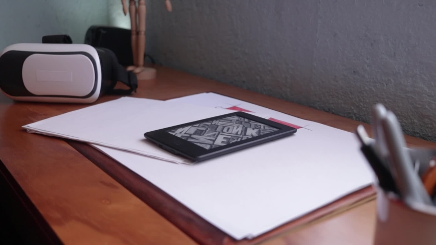 Side view. Male hand reading and turning pages on an ebook reader. Ebook reader on a wooden desk. Man switch off an ebook reader. Vr headset on background. 3d experience with a vr headset
