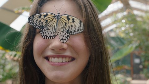 beautiful girl smiling with butterfly on face fluttering wings having fun with wildlife in nature conservation zoo 4k