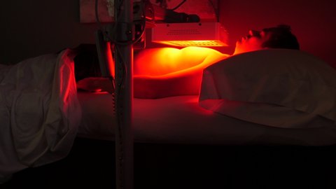 HEBER, UT, UNITED STATES, JULY 19, 2019: man sits under the red light therapy with lamp on chest. Camera remains static on patient that is lying on his back under the infrared lamp at chest level