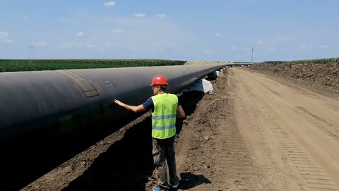 Worker With Radio Communication Device Walking at Oil Pipeline Construction Site. Engineer Checking Petrochemical Oil Pipeline at Construction Site. "Turkish Stream" Gas Pipeline Under Construction.