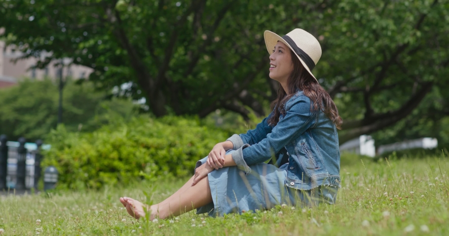 Woman sit on green lawn and look around the landscape
