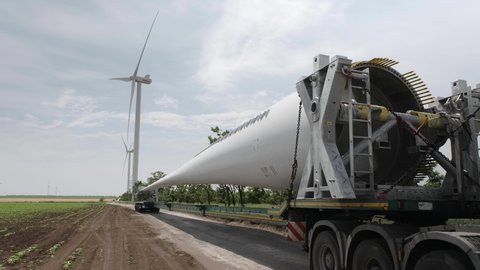 The blades of wind generators mounted on the body of long-length cargo cars against the background of the existing farm of wind power plants.