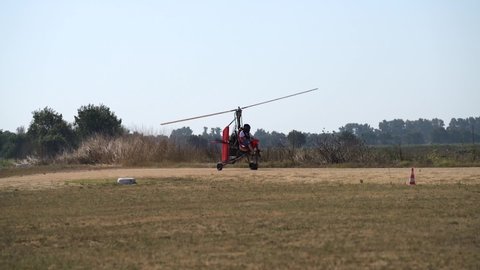 Ultralight gyrocopter autogyro with pilot picking up speed moving on unpaved runway before taking off