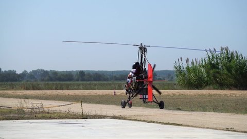 Ultralight gyrocopter autogyro with pilot picking up speed moving on unpaved runway before taking off