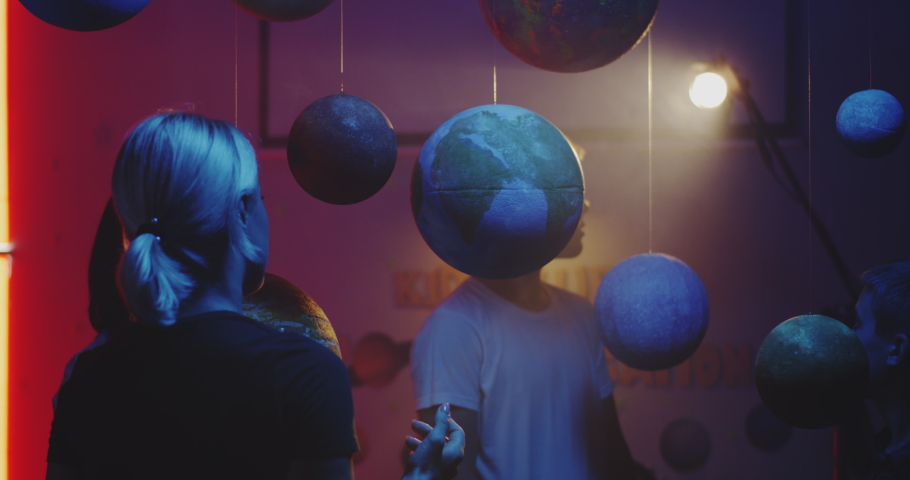 Medium shot of a female teacher explaining astronomy to students with suspended planet models