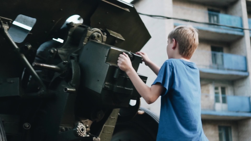 The boy stands next to the artillery. Development and education of children. Museum exhibit.