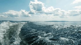 Movement by boat on the sea. Shooting from the stern. You can see the wake from the engine, the far horizon, clean air and waves, splashing water. Space for text. Atmospheric video.