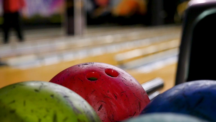 Close-up of young man taking bowling balls from the rack. Media. Competitive cheerful friends playing bowling together in the club