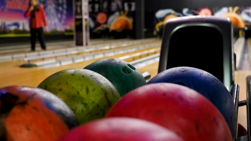Close-up of young man taking bowling balls from the rack. Media. Competitive cheerful friends playing bowling together in the club