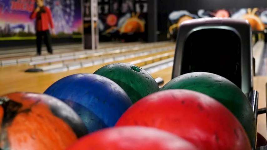 Close-up of young man taking bowling balls from the rack. Media. Competitive cheerful friends playing bowling together in the club