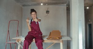 Portrait of young woman wearing workers uniform sitting on scaffolding and having lunch break. Girl making repairs in house. 4K slow motion raw video footage 60 fps