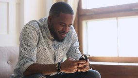 Smiling african american man holding smartphone texting sms message or play mobile game sit on sofa at home, happy young black guy using social media app work study on cell phone looking at screen - Powered by Shutterstock - Get 15% off with code: PIKWIZARD15