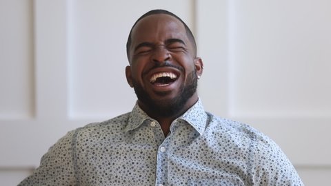 Cheerful black man happy face looking at camera and laughing at funny joke, young african american guy with wide smile having fun enjoy humor sincere laughter positive emotions sit alone at home