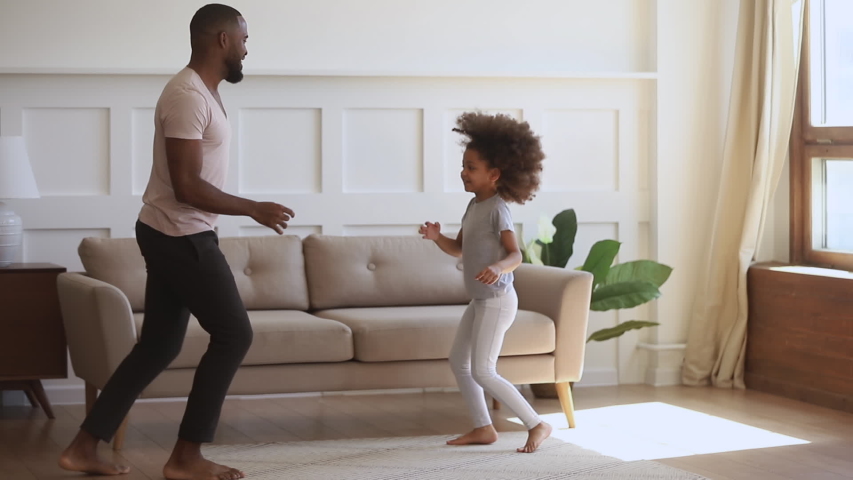 Happy funny carefree african family father and cute little kid daughter jumping having fun together in living room, dad dancing with small child girl enjoy music active morning playing at home Royalty-Free Stock Footage #1034099225