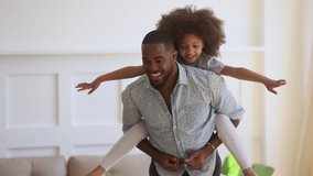 Happy family loving black dad giving cute little funny kid daughter piggyback ride spinning at home, cheerful african father carrying small child girl on back bonding having fun playing together - Powered by Shutterstock - Get 15% off with code: PIKWIZARD15