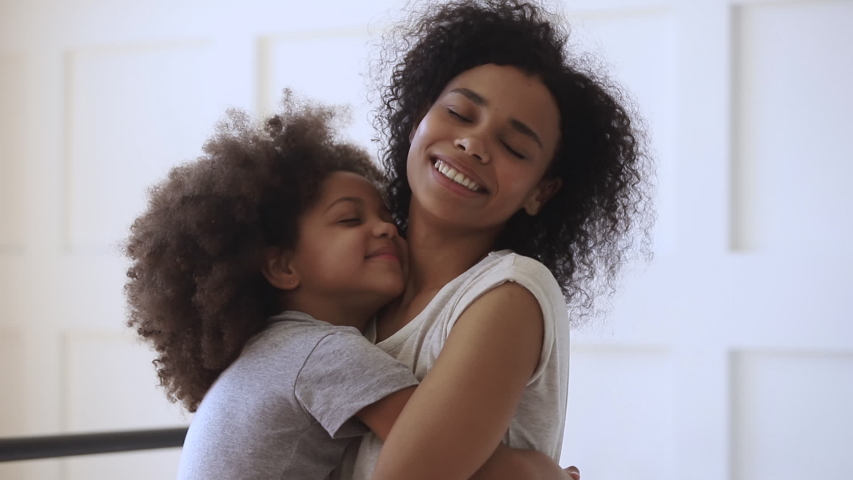 Happy loving young black mother hugging cute little child daughter holding tight cuddling looking, affectionate african american family mom foster parent embracing small kid girl bonding together Royalty-Free Stock Footage #1034099279