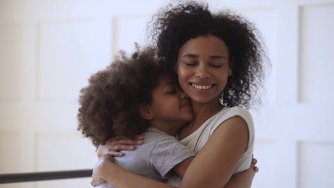 Happy loving young black mother hugging cute little child daughter holding tight cuddling looking, affectionate african american family mom foster parent embracing small kid girl bonding together