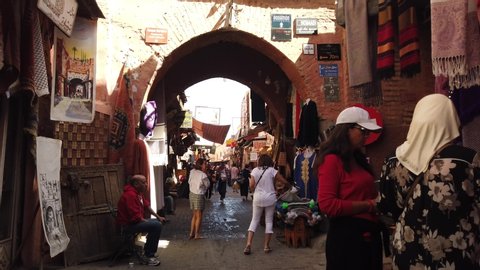 MARRAKECH, MOROCCO - APRIL 2019: Alley in the Medina with local market vendors and tourists walking. POV Walking.