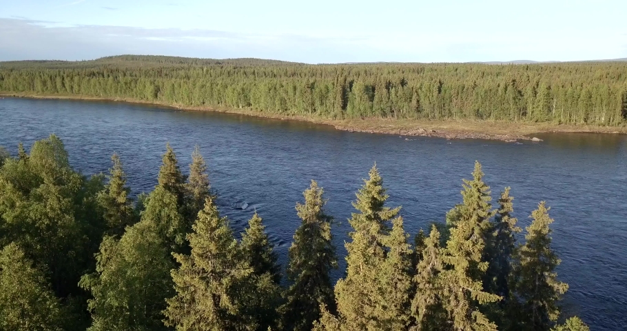 Aerial, drone shot, panning around finnish forest, overlooking the Tornionjoki river, on a sunny day, in Pello, Meri-Lappi, Lapland, Finland