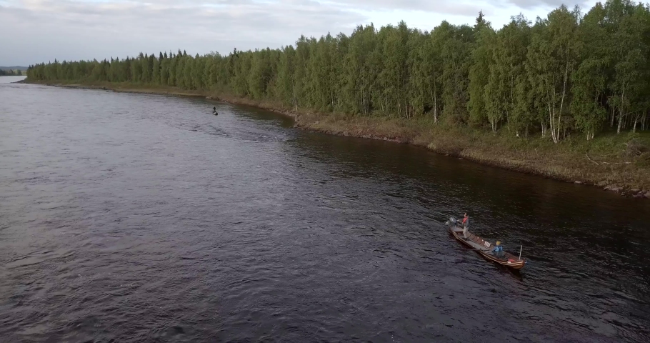 Aerial, reverse, drone shot, of a fishing boat on the Tornionjoki river, on a cloudy day, in Pello, Meri-Lappi, Lapland, Finland