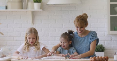 Cute funny children daughters and mother having fun cooking play with flour in kitchen, happy mum teach kids siblings help prepare dough for cookie with rolling pin together learn bake pastry at home