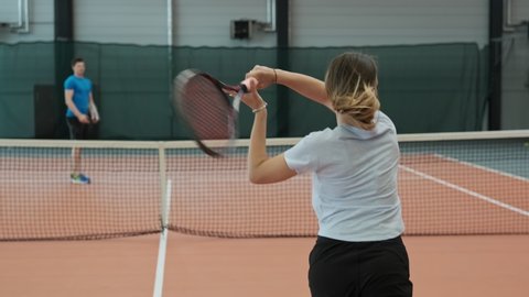 Young people playing tennis in slow motion. Beautiful woman in sportswear and long hair making wide serve ball in tennis. Medium shot of female tennis player serving.
