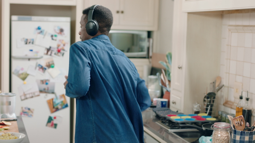 happy african american man dancing in kitchen listening to music wearing headphones having fun dance celebration enjoying weekend at home