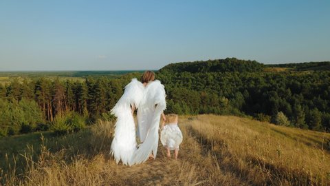 Rear view: A woman with a child dressed as angels walk in nature in the highlands. Slow motion video
