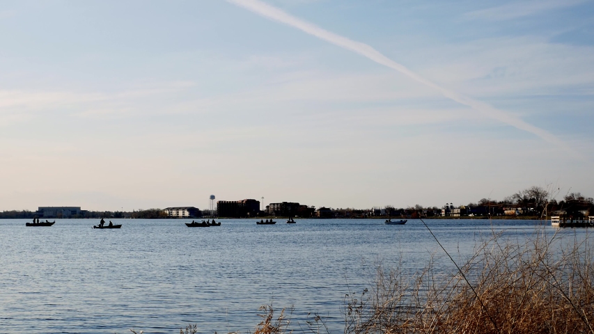 People fishing in motor boats on Lake Bemidji near the Mississippi River on the morning of Minnesota Fishing Opener with buildings and traffic on far shore. Zoom in and pan right.