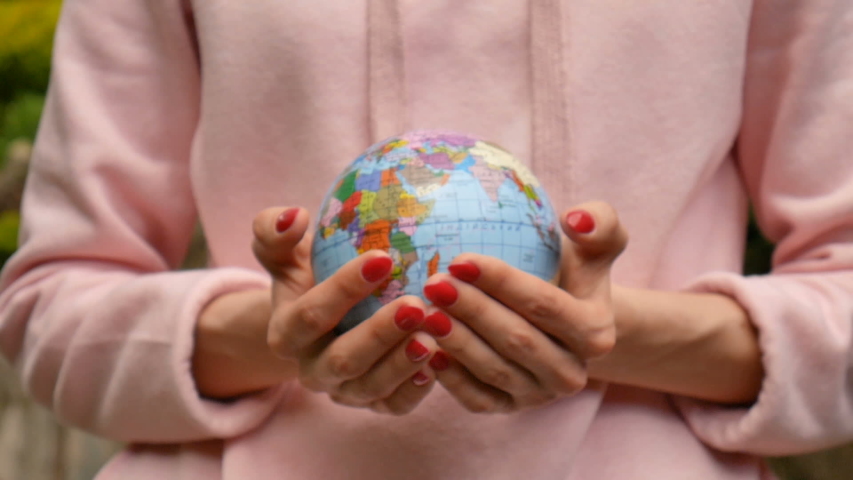 Close up video of female hands with red manicure giving a small globe with geographical names in Ukrainian cyrillic letters on it. Eco friendly lifstyle concept