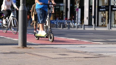 Düsseldorf, Germany - JULY 2019: People walk cross the road, cyclist and rider ride bicycle and E-scooter on bicycle lane at pedestrian crossing and blur background of cityscape at Königsallee.