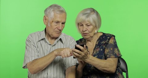 Senior aged man and woman sitting together and working on smartphone. Grandmother and grandfather. Chroma key background. Concept of a happy family in old age. Green screen background