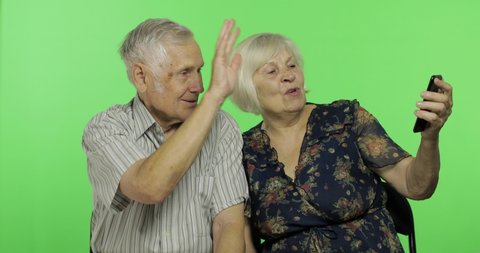 Senior aged man and woman sitting together and talks on a smartphone. Having video chat using smartphone. Grandmother and grandfather. Chroma key background. Green screen background