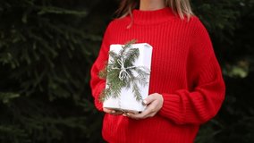 woman in red sweater with christmas gift near pine tree