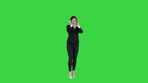 Young business woman listening to music in headphones and dancing on a Green Screen, Chroma Key.