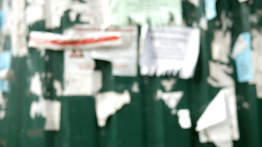Blurred abstract background with worn advertising message on metal fence. Outdoors.