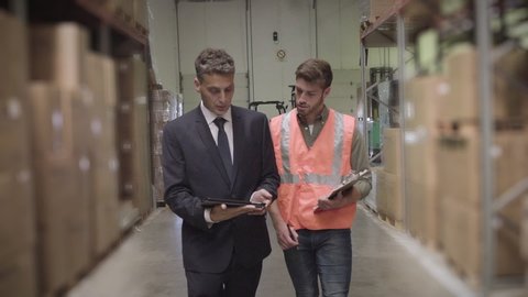 Medium shot of warehouse worker and businessman discussing with digital tablet and clipboard while maintaining records in warehouse